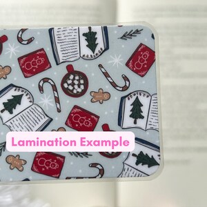 May include: A blue and white patterned bookmark with images of books, candy canes, hot chocolate, and snowmen. The text "Lamination Example" is printed on the bookmark.