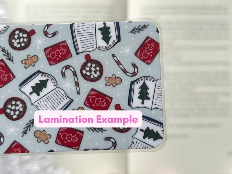 May include: A blue and white patterned bookmark with images of books, candy canes, hot chocolate, and snowmen. The text "Lamination Example" is printed on the bookmark.