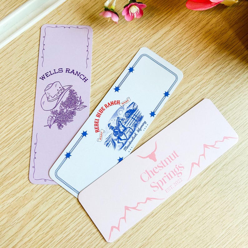 May include: Three rectangular bookmarks with Western-themed designs. One is lavender with a cowboy hat and floral illustration, another is white with a blue illustration of a cowboy on a horse, and the last is pink with text.