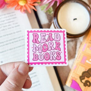 Peut inclure: Autocollant rose et blanc avec le texte "READ MORE BOOKS" dans une police rétro avec des pois blancs. L'autocollant est sur un fond blanc.