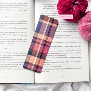 K&ouml;nnte beinhalten: Ein kariertes Lesezeichen in Rosa-, Lila- und Beiget&ouml;nen liegt auf den Seiten eines Buches. Das Lesezeichen hat eine rechteckige Form mit abgerundeten Ecken. Das Wort "Inverness" ist auf einem wei&szlig;en Etikett aufgedruckt.