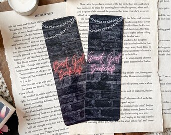 May include: Two black bookmarks with a brick wall background and a neon sign that reads "Bad Girl Bookclub" in pink and "Good Girl Bookclub" in red. The bookmarks feature a silver chain design.