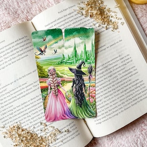May include: Two illustrated bookmarks featuring a green and pink path leading to a city in the distance. The bookmark on the left features a woman with long blonde hair wearing a pink dress and the bookmark on the right features a woman with long black hair wearing a green dress. The text "Rock Paper Scissors" is visible in the background.