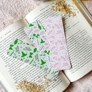 May include: Two bookmark designs featuring a green witch and a pink witch. The green witch bookmark has a green hat and the text "Team Elphaba" repeated on the bookmark. The pink witch bookmark has a pink crown and the text "Team Glinda" repeated on the bookmark.