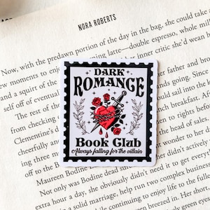 May include: A white sticker with black borders features a black and white illustration of a heart pierced by a dagger with a crown of thorns. The text "DARK ROMANCE" is in black with white stars above and below the text. The text "Book Club" is in black with the text "Always falling for the villain" in smaller font below.