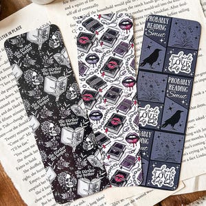 Peut inclure: Trois marque-pages avec des motifs différents. Le premier marque-page présente un motif noir et blanc de crânes, de livres et de chaînes. Le deuxième marque-page présente un motif noir et blanc de livres, de lèvres et de chaînes. Le troisième marque-page présente un motif noir et blanc d'un corbeau, de fleurs et du texte "Good girls love to read smut".
