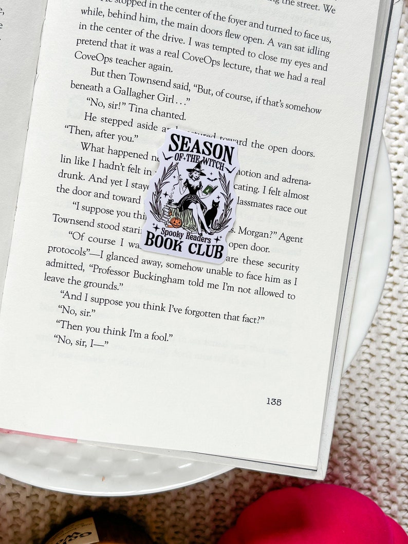 May include: A black and white sticker with a witch holding a black cat. The sticker says "Season of the Witch" and "Spooky Readers Book Club".