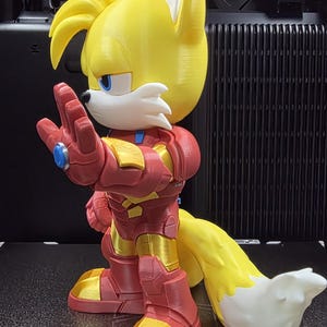 Op de afbeelding: Een 3D-geprint figuur van Tails uit Sonic the Hedgehog, in een op Iron Man ge&iuml;nspireerd pak. Het figuur is geel, rood en goud, met een witte en gele staart. Het figuur staat op een oppervlak van 320 x 325 mm.