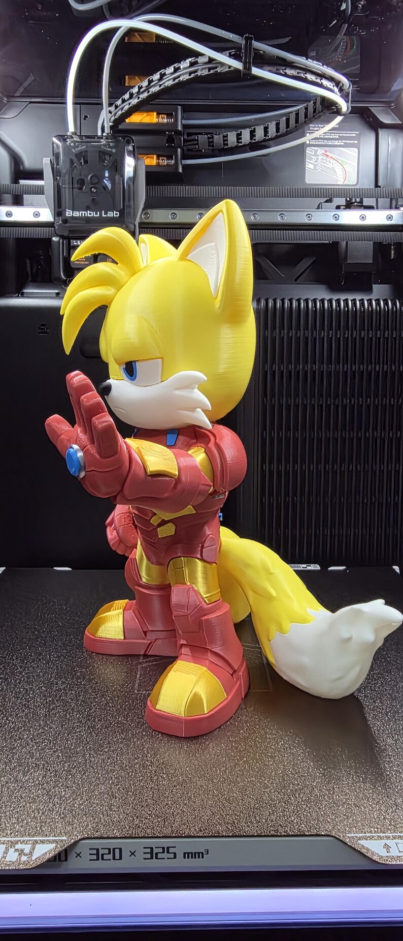 Op de afbeelding: Een 3D-geprint figuur van Tails uit Sonic the Hedgehog, in een op Iron Man ge&iuml;nspireerd pak. Het figuur is geel, rood en goud, met een witte en gele staart. Het figuur staat op een oppervlak van 320 x 325 mm.