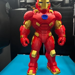 Op de afbeelding: Een 3D-geprinte Iron Man-actiefiguur met een rood en goudkleurig pak en een blauwe arc-reactor op de borst. Het figuur heeft een goudkleurig masker, gedetailleerde bepantsering en staat in een neutrale houding met een robuust ontwerp.