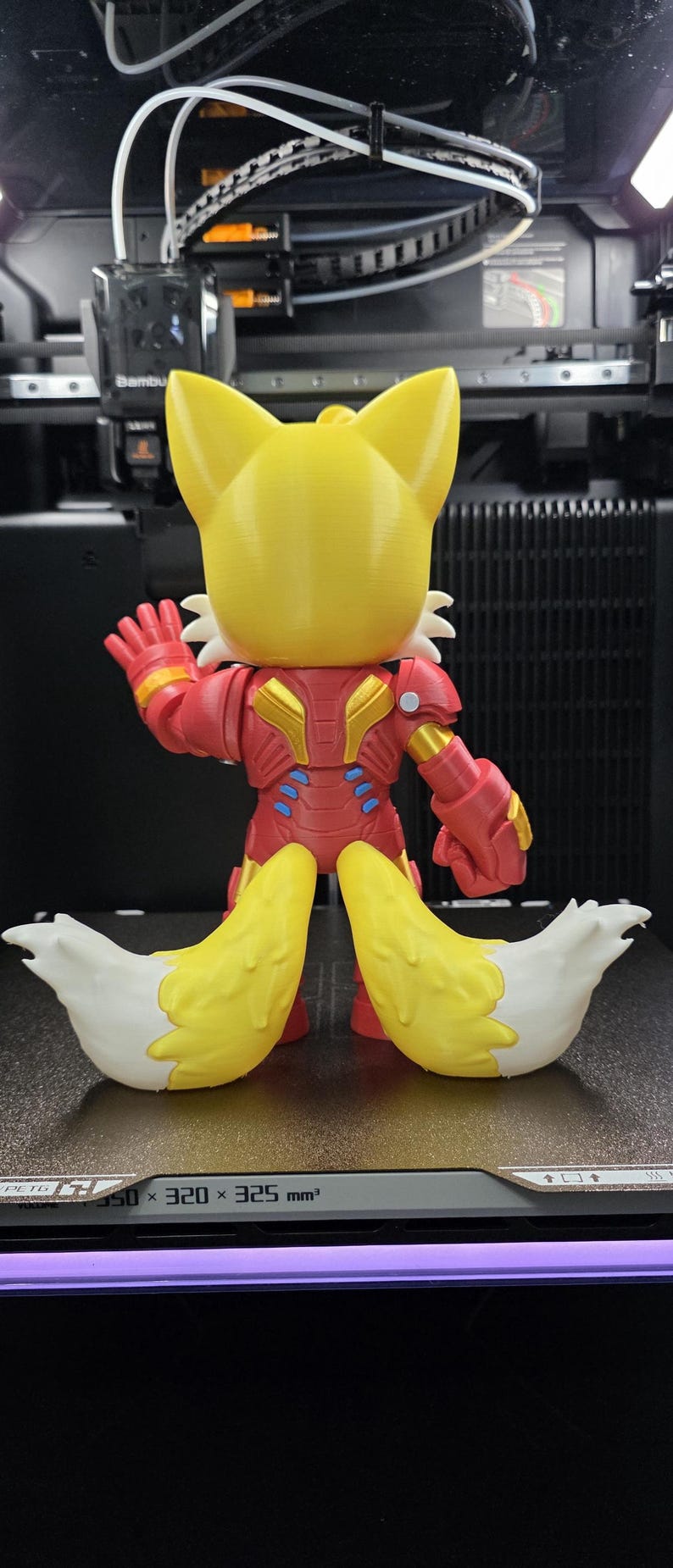 Op de afbeelding: Een 3D-geprint beeldje van een vos-personage in een rood en goudkleurig Iron Man-achtig pak. De vos heeft gele oren en een gele kop, met twee grote, pluizige, geel en witte staarten. De figuur poseert met &eacute;&eacute;n hand omhoog.