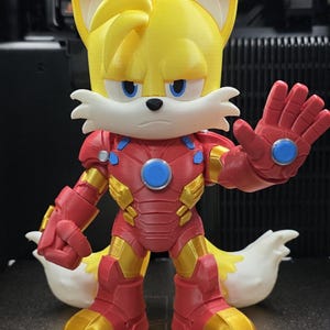 Op de afbeelding: Een 3D-geprint beeldje van Tails uit Sonic the Hedgehog, gekleed in een Iron Man-pak. De figuur is geel, rood en goud, met blauwe accenten. De figuur staat met &eacute;&eacute;n hand omhoog.