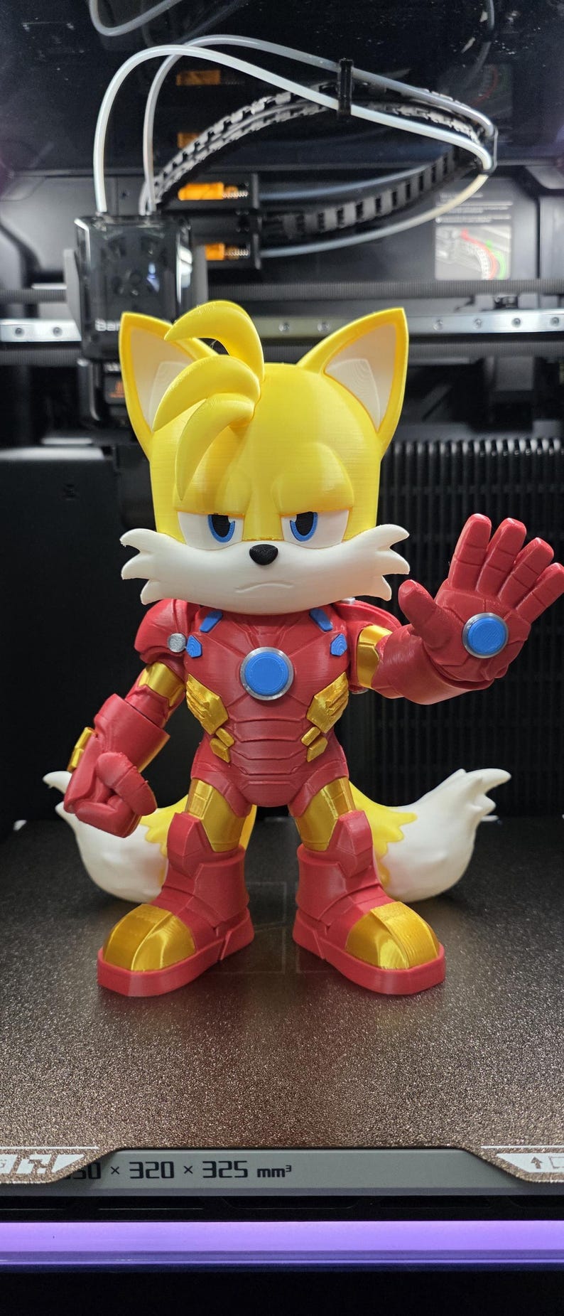 Op de afbeelding: Een 3D-geprint beeldje van Tails uit Sonic the Hedgehog, gekleed in een Iron Man-pak. De figuur is geel, rood en goud, met blauwe accenten. De figuur staat met &eacute;&eacute;n hand omhoog.
