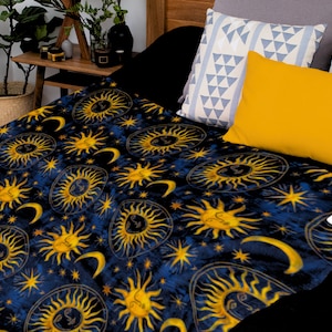 May include: A blue fleece throw blanket with a repeating pattern of gold suns and moons on a dark blue background.