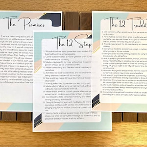 May include: Three printed cards with the text "The Promises", "The 12 Steps", and "The 12 Traditions" on a wooden surface. The cards are printed with a light blue, pink, and white background.