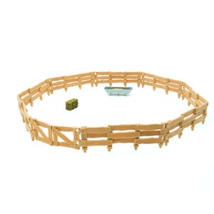 May include: A wooden fence with a hay bale and a metal trough inside. The fence is made of brown wooden planks and is arranged in a circular shape.