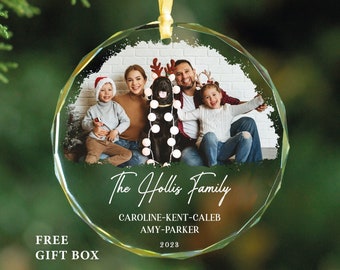 May include: A round, clear glass Christmas ornament with a family photo inside. The photo shows a family of four with a dog. The ornament has a white background with black text that reads "The Hollis Family", "CAROLINE-KENT-CALEB", "AMY-PARKER", and "2023".