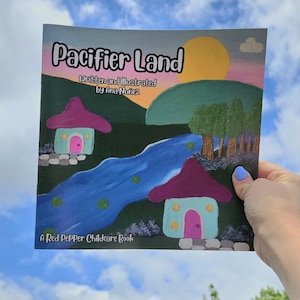 May include: A children's book titled "Pacifier Land" with colorful illustrations of houses, a river, and a sunset. The book is written and illustrated by Ana Nunez and published by A Red Pepper Childcare Book.