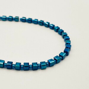 May include: A blue beaded bracelet made of square-shaped beads.