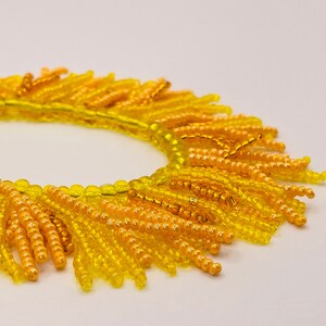 May include: A yellow and orange beaded bracelet with a fringe design. The bracelet is made of small, round beads that are strung together to create a circular shape. The fringe is made of longer beads that hang down from the bottom of the bracelet.