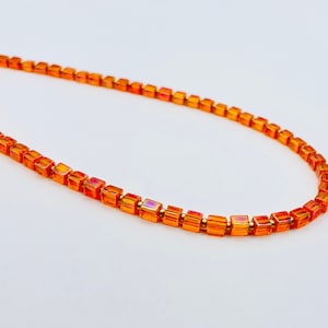 Peut inclure: Un collier composé de petites perles carrées orange irisées.