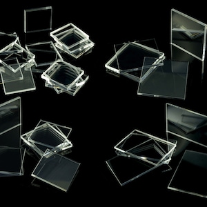 Könnte beinhalten: Eine Sammlung von durchsichtigen Acrylquadraten und -rechtecken in verschiedenen Größen, die auf einem schwarzen Hintergrund gestapelt und verstreut sind.