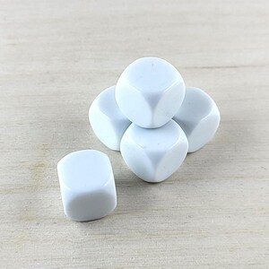 Puede incluir: Cinco dados blancos, apilados en forma de pir&aacute;mide, sobre una superficie de madera clara.