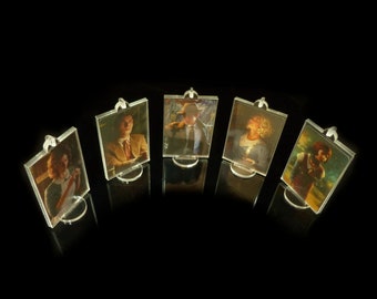 Pode incluir: Cinco molduras de fotos de acrílico transparente com um laço para pendurar na parte superior. Cada moldura contém uma fotografia vintage diferente de uma pessoa. As molduras estão dispostas em semicírculo sobre uma superfície preta.