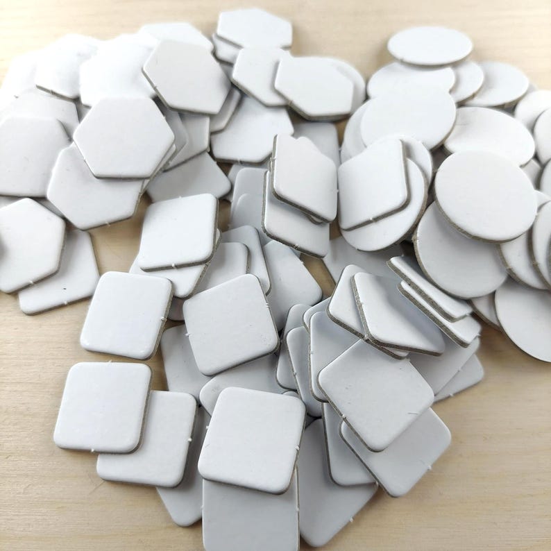 Puede incluir: Una colecci&oacute;n de piezas de artesan&iacute;a blancas de formas geom&eacute;tricas, incluyendo cuadrados, hex&aacute;gonos y c&iacute;rculos. Las piezas est&aacute;n apiladas sobre una superficie de madera clara, creando un efecto texturizado y en capas. Las formas tienen una est&eacute;tica limpia y minimalista.