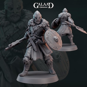 Könnte beinhalten: Eine graue Plastik-Miniaturfigur eines Kriegers mit einem gehörnten Helm, einem pelzgefütterten Umhang und einem Schild und einer Axt. Die Figur steht auf einem runden Sockel.
