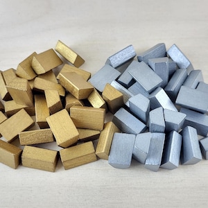 May include: A pile of gold and silver wooden blocks. The blocks are all the same size and shape, but they are different colors. The gold blocks are on the left side of the image, and the silver blocks are on the right side of the image.