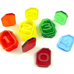 May include: A set of eight acrylic number tokens in various colours, including red, yellow, green, and blue. Each token is shaped like a hexagon and features a white number from 0 to 7.