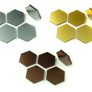 May include: A selection of hexagonal tiles in three colours: grey, gold, and brown. Each tile has a reflective surface, and some are positioned to show their side profile. The tiles are arranged on a white background.