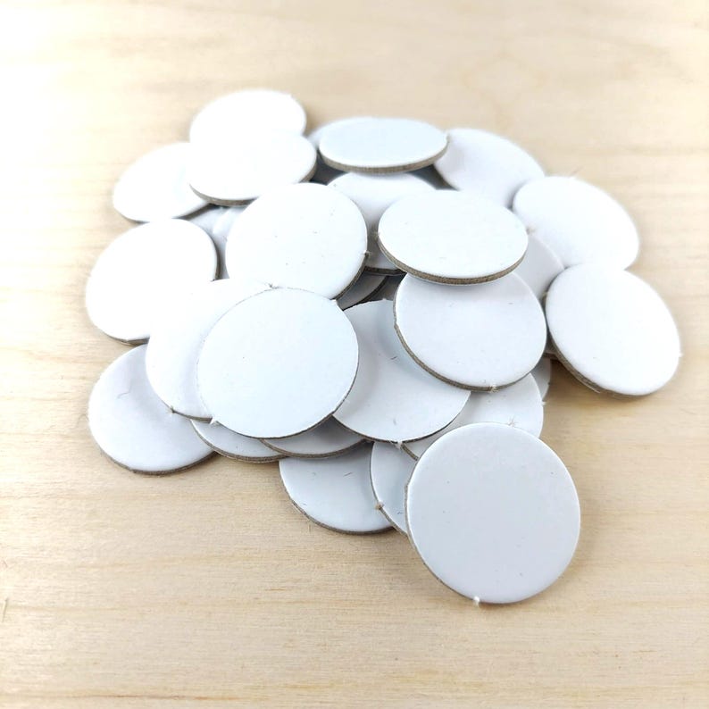 Puede incluir: Un mont&oacute;n de peque&ntilde;os c&iacute;rculos de cart&oacute;n blancos. Los c&iacute;rculos tienen una superficie blanca y un borde marr&oacute;n claro. Los objetos est&aacute;n dispersos sobre una superficie de madera clara.