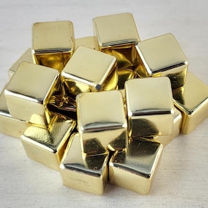 May include: A pile of small, gold-coloured metal cubes. The cubes are arranged in a random pattern, with some cubes stacked on top of others.