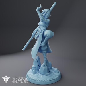 May include: A light blue unpainted resin miniature figure of a warrior standing on a rock formation base with a circular rippled water design. The figure holds a long staff, wears wrapped arm guards, and has a flowing garment with a tied waist sash.