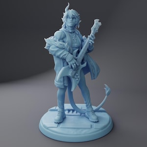 Pode incluir: Estatueta azul clara de um personagem tocando guitarra elétrica. O personagem tem chifres, uma cauda e usa jaqueta e botas. A estatueta está em uma base redonda.