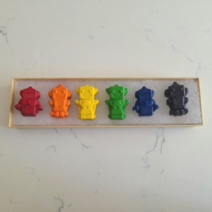 May include: A set of six crayon robots in a rainbow of colours, red, orange, yellow, green, blue, and purple, in a wooden box.