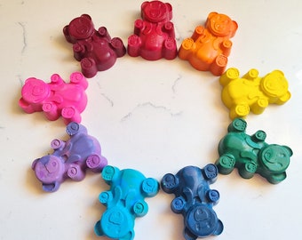 May include: A set of nine colorful bear-shaped crayons in a rainbow color scheme. The crayons are arranged in a circle with the red crayon at the top.