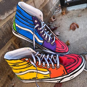 May include: A pair of high-top sneakers with a vibrant, cartoon-like design. One shoe features a blue and purple upper, while the other showcases yellow, orange, and red hues. Both have white laces and soles, creating a bold, eye-catching look.