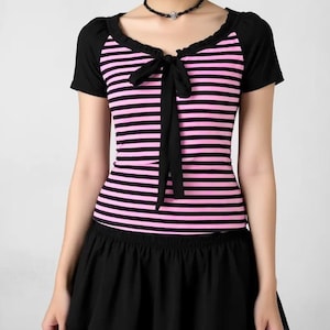 May include: A black and pink striped top with a black bow and a black skirt. The top has short sleeves and a scoop neckline. The skirt is a short, flared style. The outfit is a combination of casual and feminine elements.