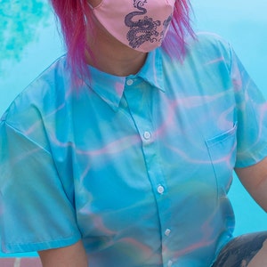 May include: A blue and pink tie-dye button-up shirt with short sleeves. The shirt has a pocket on the left side and a white button closure.