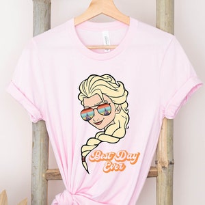 Puede incluir: Camiseta rosa con una imagen de dibujos animados de una mujer con cabello rubio usando gafas de sol y el texto "Best Day Ever".