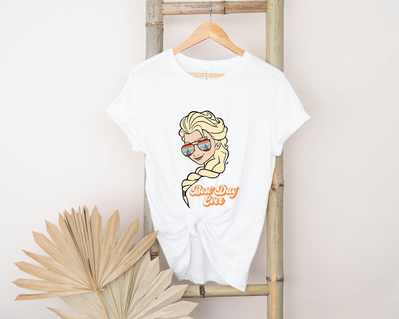 Puede incluir: Camiseta blanca con una imagen de dibujos animados de Elsa de Frozen con gafas de sol y el texto "Best Day Ever".