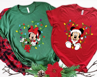 May include: Two Christmas themed t-shirts featuring Mickey Mouse and Minnie Mouse. The green shirt has Minnie Mouse holding a wreath with a red bow. The red shirt has Mickey Mouse wearing a Santa hat and holding Christmas lights.