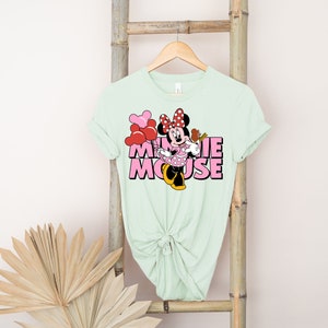 May include: A light green t-shirt with a pink and red graphic of Minnie Mouse with the text "Minnie Mouse" in pink letters.