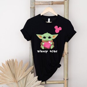 May include: Black t-shirt featuring a green Baby Yoda character holding a pink heart and the text "Disney Mode".