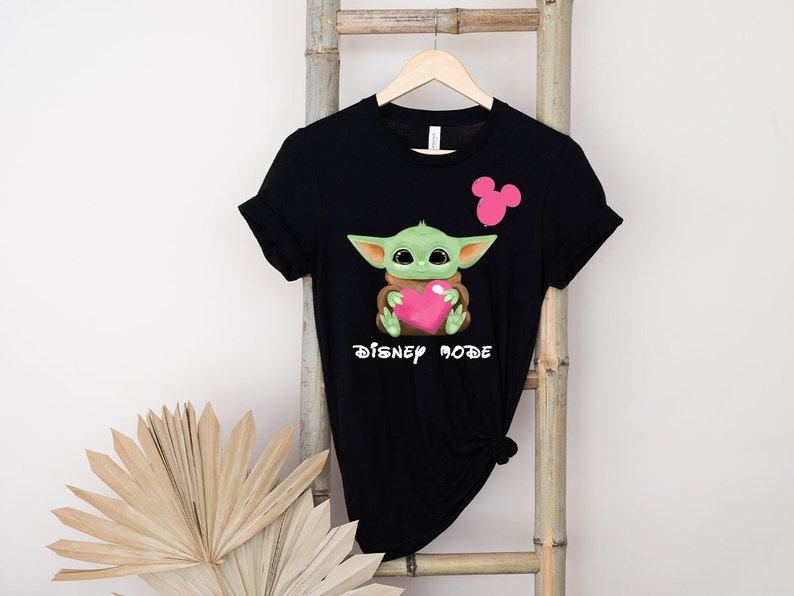 May include: Black t-shirt featuring a green Baby Yoda character holding a pink heart and the text "Disney Mode".