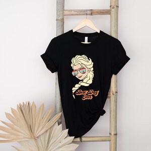 Puede incluir: Camiseta negra con un gr&aacute;fico de un personaje de dibujos animados con cabello rubio que lleva gafas de sol y el texto "Best Day Ever".