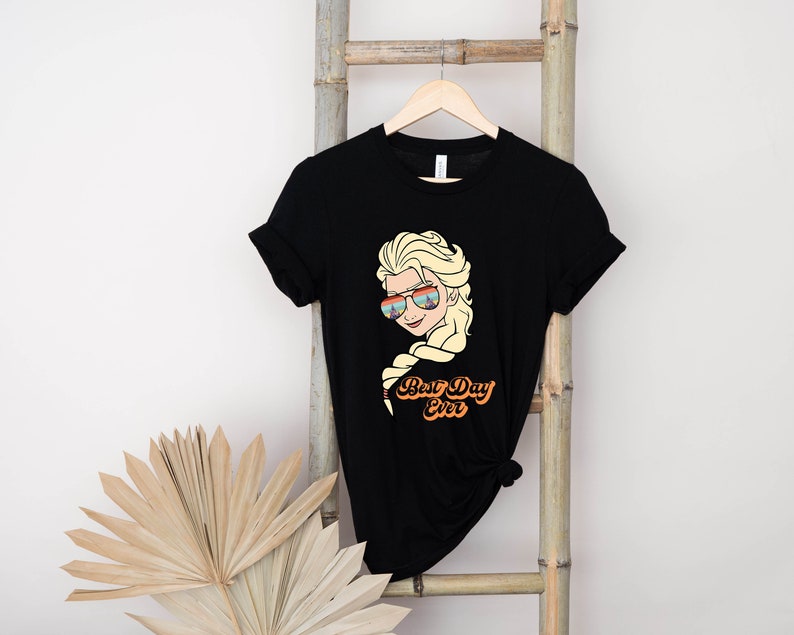 Puede incluir: Camiseta negra con un gr&aacute;fico de un personaje de dibujos animados con cabello rubio que lleva gafas de sol y el texto "Best Day Ever".